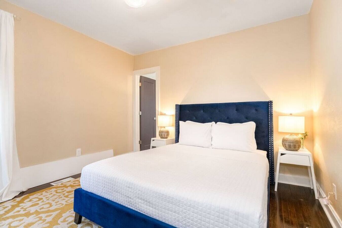 Habitación de hotel con cama, dos mesitas de noche, una puerta y una alfombra estampada.