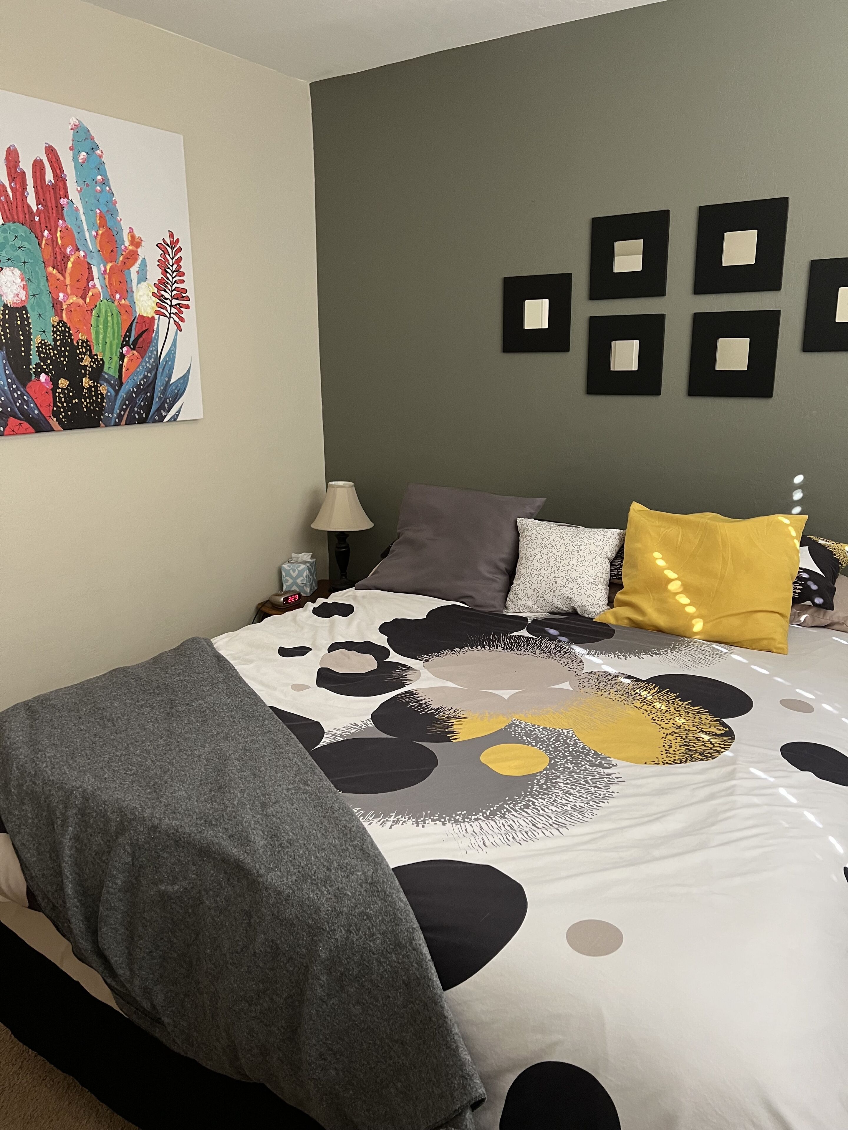 Une chambre à coucher avec un lit, des oreillers, une table de chevet, une lampe et une œuvre d’art murale.
