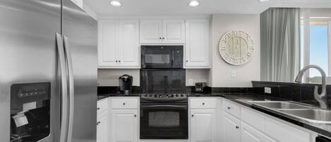 A modern kitchen with white cabinets, stainless steel appliances, a black countertop, and a large wall clock.