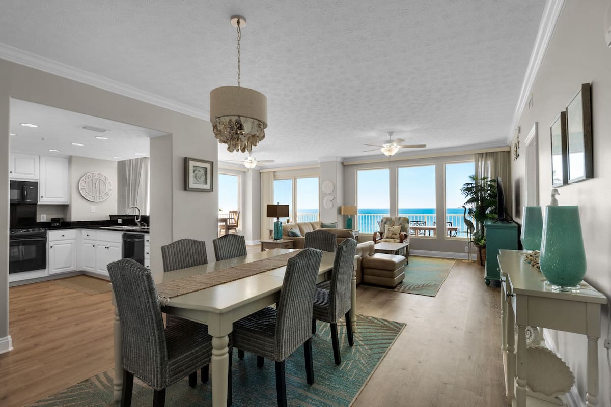 A spacious living area with a dining table, chairs, and a view of the ocean.