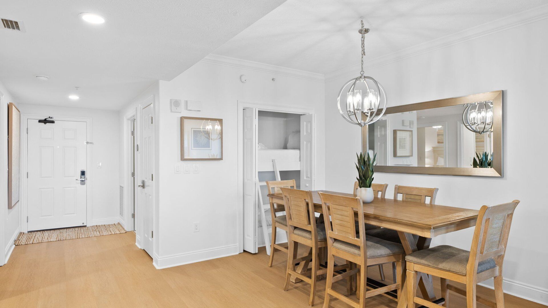 A dining area with a wooden table and chairs, a chandelier, and a large mirror on the wall.