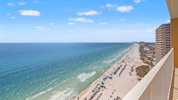 A beach view from a balcony overlooking a sandy beach with umbrellas and a hotel building.