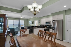 A spacious kitchen with white cabinets, a stainless steel refrigerator, and a dining area with wooden chairs and a glass table.