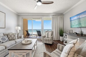 A living room with a sofa, armchair, coffee table, and a view of the ocean through large sliding doors. - Treasure Island 0209 (Panama City Beach)