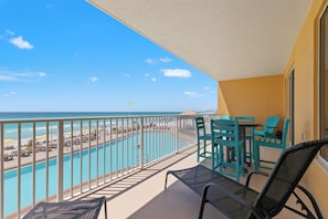 A balcony with a view of a swimming pool and beach, turquoise chairs, and a table. - Treasure Island 0209 (Panama City Beach)