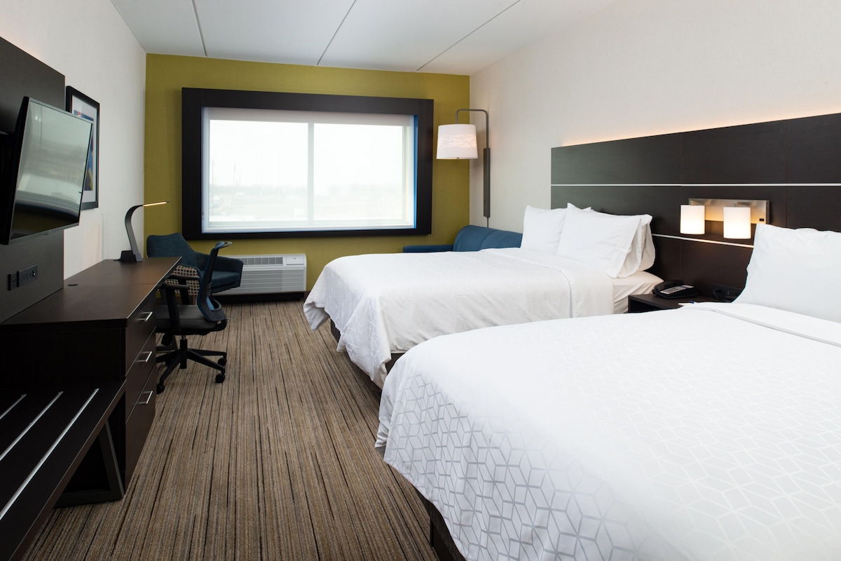 A hotel room with two beds, a desk, a chair, a TV, and a large window.