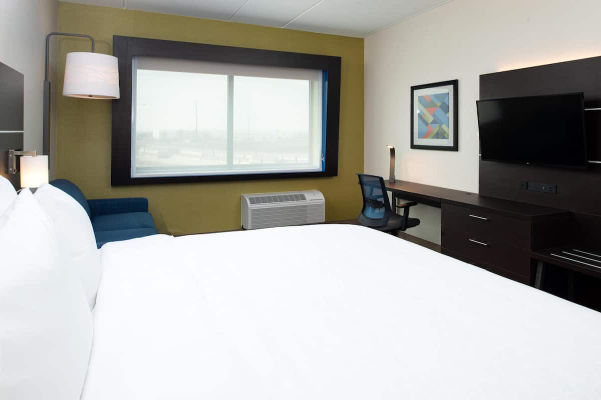 Habitación de hotel con cama, escritorio, silla, televisor, ventana y aire acondicionado instalado en la pared.