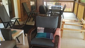 Ein überdachter Patio-Bereich mit Korbmöbeln, einem gemusterten Teppich und einem dekorativen Wandbild.