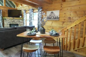 Un intérieur en bois comprenant une table à manger, des chaises, un canapé, un téléviseur et une cheminée.