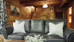 Interior de una cabaña de madera con un sofá de cuero, un reloj y un cuadro en la pared.