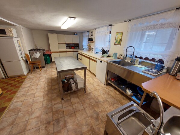 Een kleine keuken met eenvoudige apparatuur, een eethoek en een raam met kantgordijnen.
