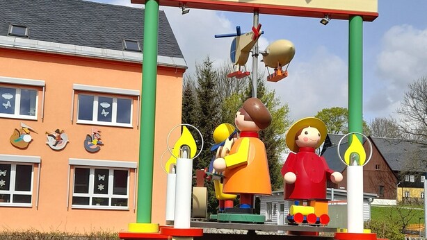 Une enseigne d’accueil représentant un moulin à vent et deux personnages, placée devant un bâtiment doté de fenêtres et d’une autre enseigne.