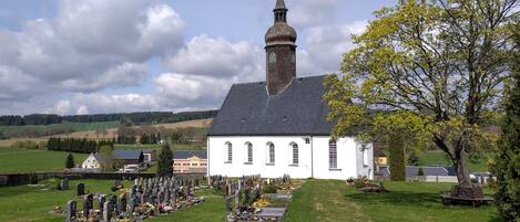 A church with a tall steeple and a cemetery in front.