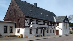 Il s’agit d’un bâtiment traditionnel à colombages, doté d’un toit à pignon très incliné, d’une petite construction adjacente avec un toit plat et d’une rue pavée devant.