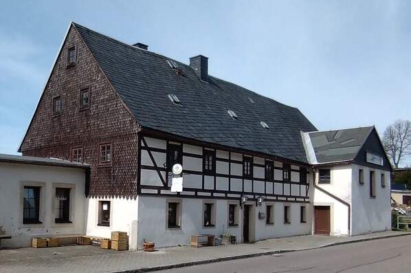 A traditional half-timbered building with a steep gable roof, a small attached white building, and a paved street in front.