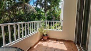 A balcony with a white railing, a potted plant, and a view of greenery.