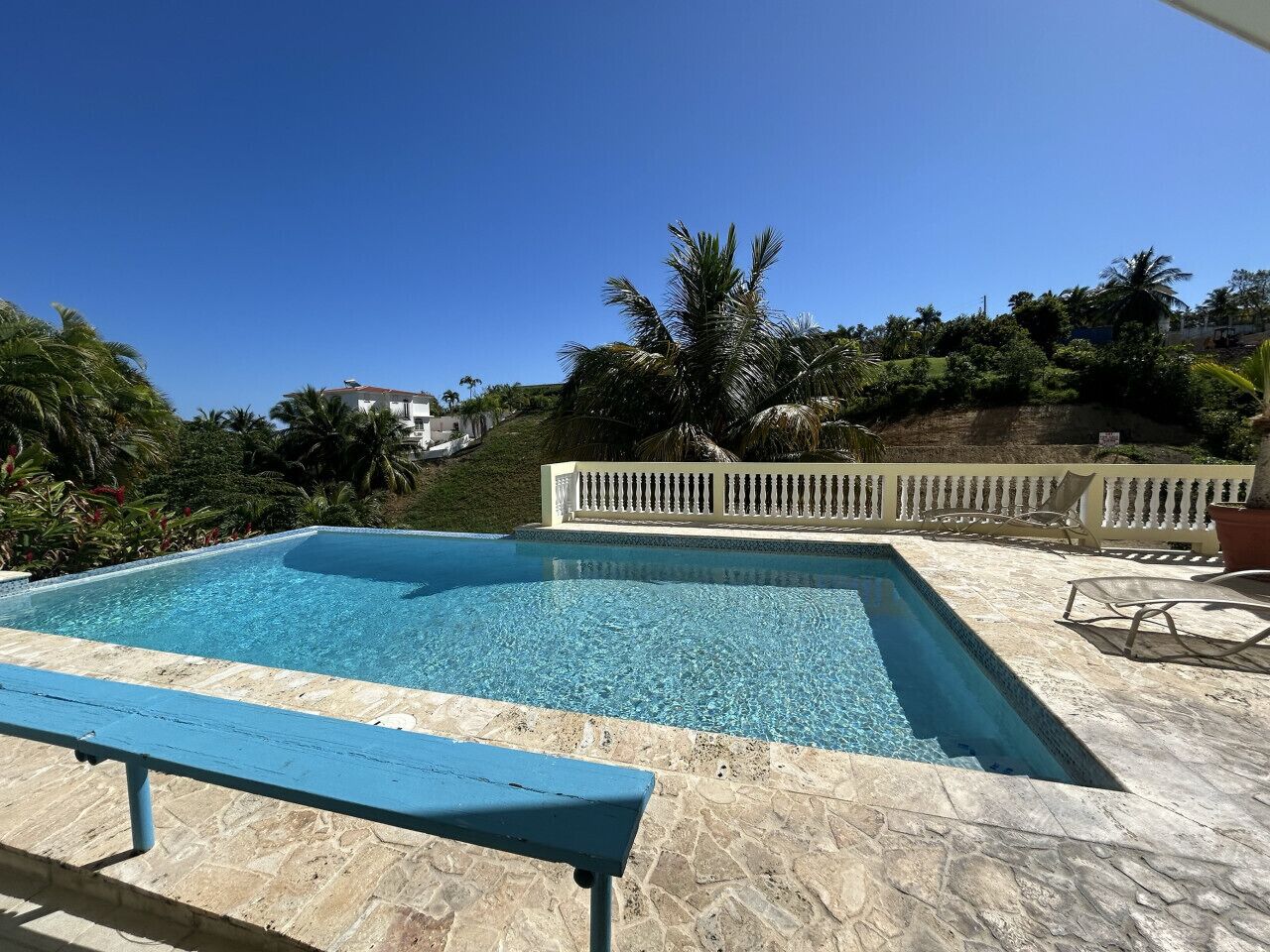 Une piscine rectangulaire à l’eau d’un bleu cristallin, entourée d’une terrasse en pierre et d’une clôture blanche.