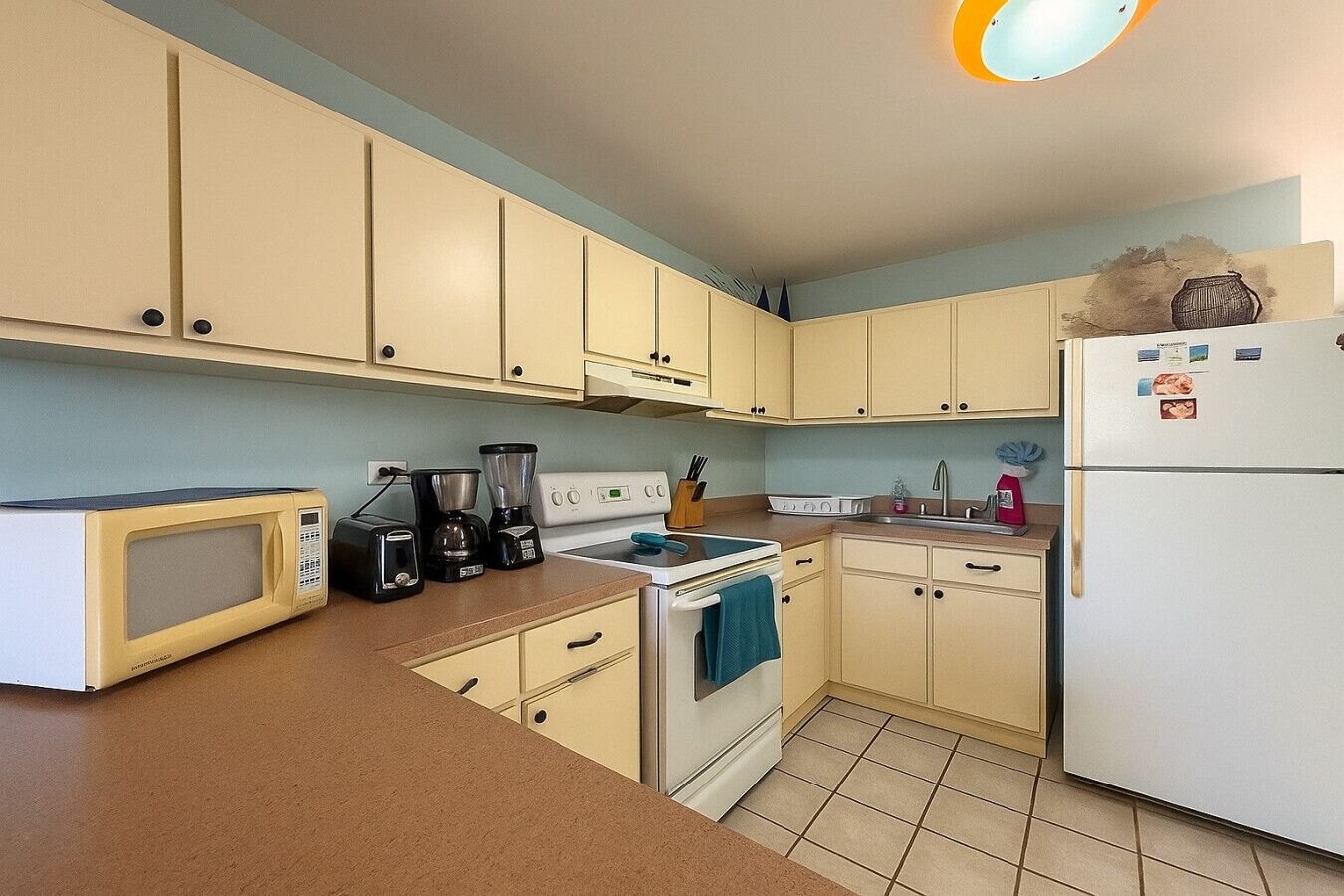 A compact kitchen with beige cabinets, a microwave, a coffee maker, a stove, and a refrigerator.