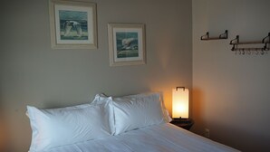 A neatly made bed with white bedding, two framed pictures on the wall, and a bedside lamp. - Grub House Coffee & Cabins (Island Park)