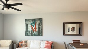 A living room with a wicker sofa, a coffee table, a dining table with chairs, a ceiling fan, and artwork on the wall. - Ocean Terrace 202 a 4 min walk to Sandy Beach (Rincon)