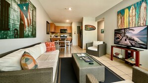 A living room with a sofa, coffee table, and chairs, a dining area with a table and chairs, a kitchen with cabinets and appliances, and a TV on a stand. - Ocean Terrace 202 a 4 min walk to Sandy Beach (Rincon)