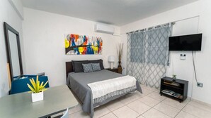A modern bedroom with a bed, a desk, a TV, and a bookshelf. - Green Mountain Studio #1 (Rincón)
