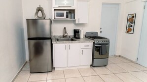 A compact kitchen with a stainless steel refrigerator, a microwave, a gas stove, and white cabinets. - Green Mountain Studio #1 (Rincón)