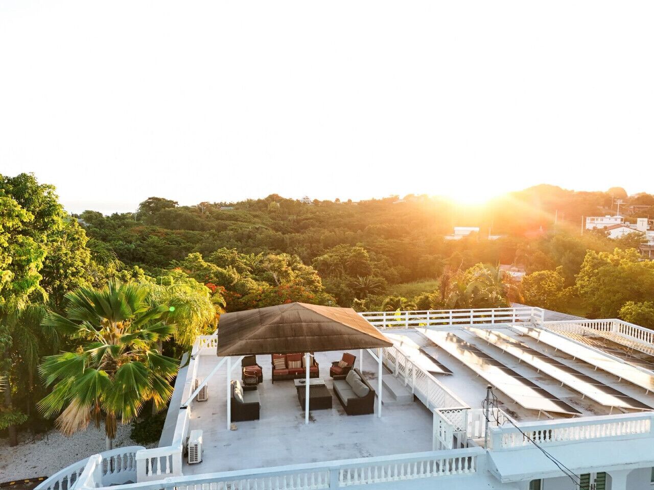 A rooftop terrace with a covered seating area, white railings, and a view of a lush green landscape.