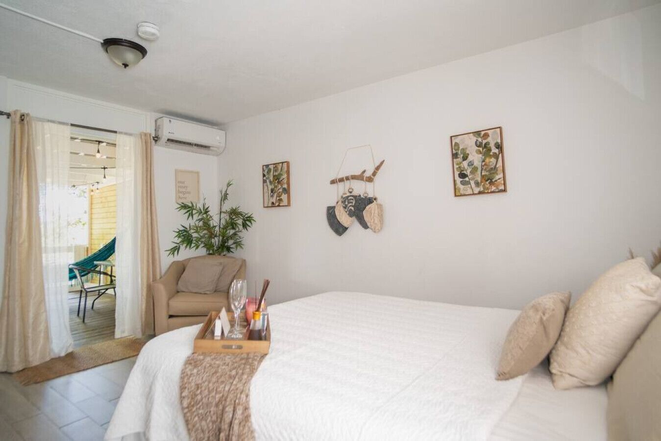A bedroom with a large bed, a chair, a small table with a tray, and a potted plant.