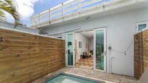 Un espace piscine entouré d’une clôture en bois, une porte vitrée donnant sur une pièce et un balcon avec une balustrade.
