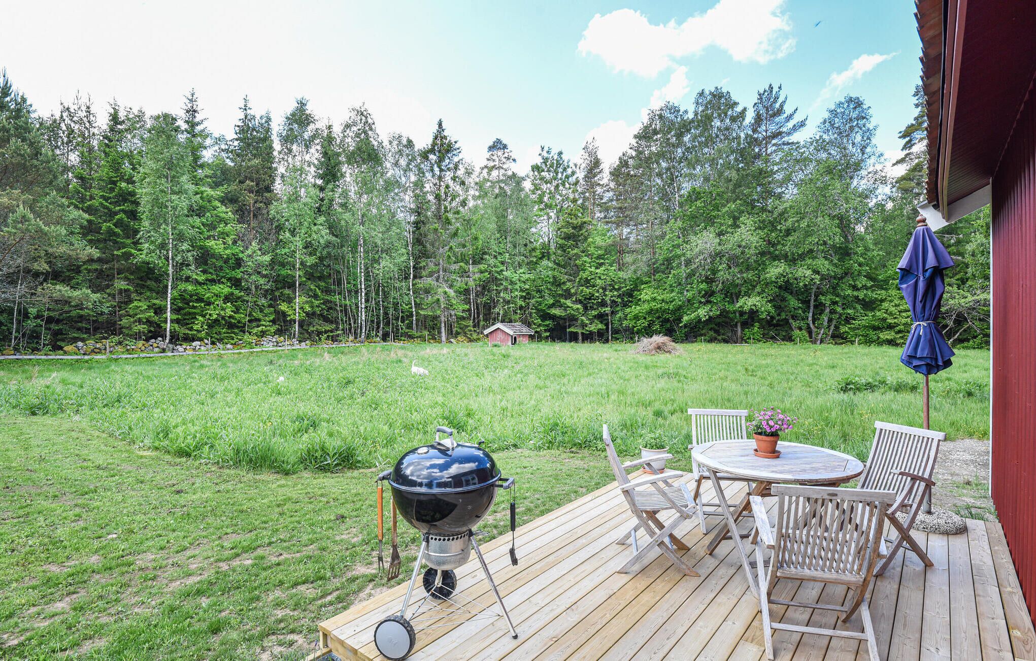 Una terraza de madera con una parrilla, sillas y una mesa.