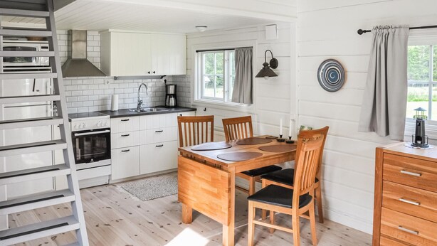A modern kitchen with white cabinets, a built-in oven, and a dining area with a wooden table and chairs. - Pet friendly home in Stillingsön (Stillingsön)