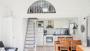 A compact kitchen with white cabinets, a stove, and a microwave. There is a wooden dining table with chairs. A ladder leads to a lofted sleeping area. - Pet friendly home in Stillingsön (Stillingsön)