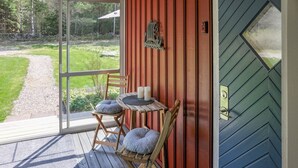A wooden deck with two chairs and a table, a glass door leading to a garden, and a metal door with a keyhole. - Pet friendly home in Stillingsön (Stillingsön)