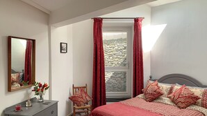A bedroom with a bed, a chair, a dresser, a mirror, and a window with curtains. - 1 bedroom accommodation in Bowness (Bowness)