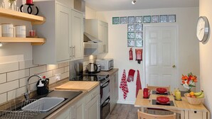A modern kitchen with white cabinets, a sink, a stove, and a dining area with a table set for two. - 1 bedroom accommodation in Bowness (Bowness)