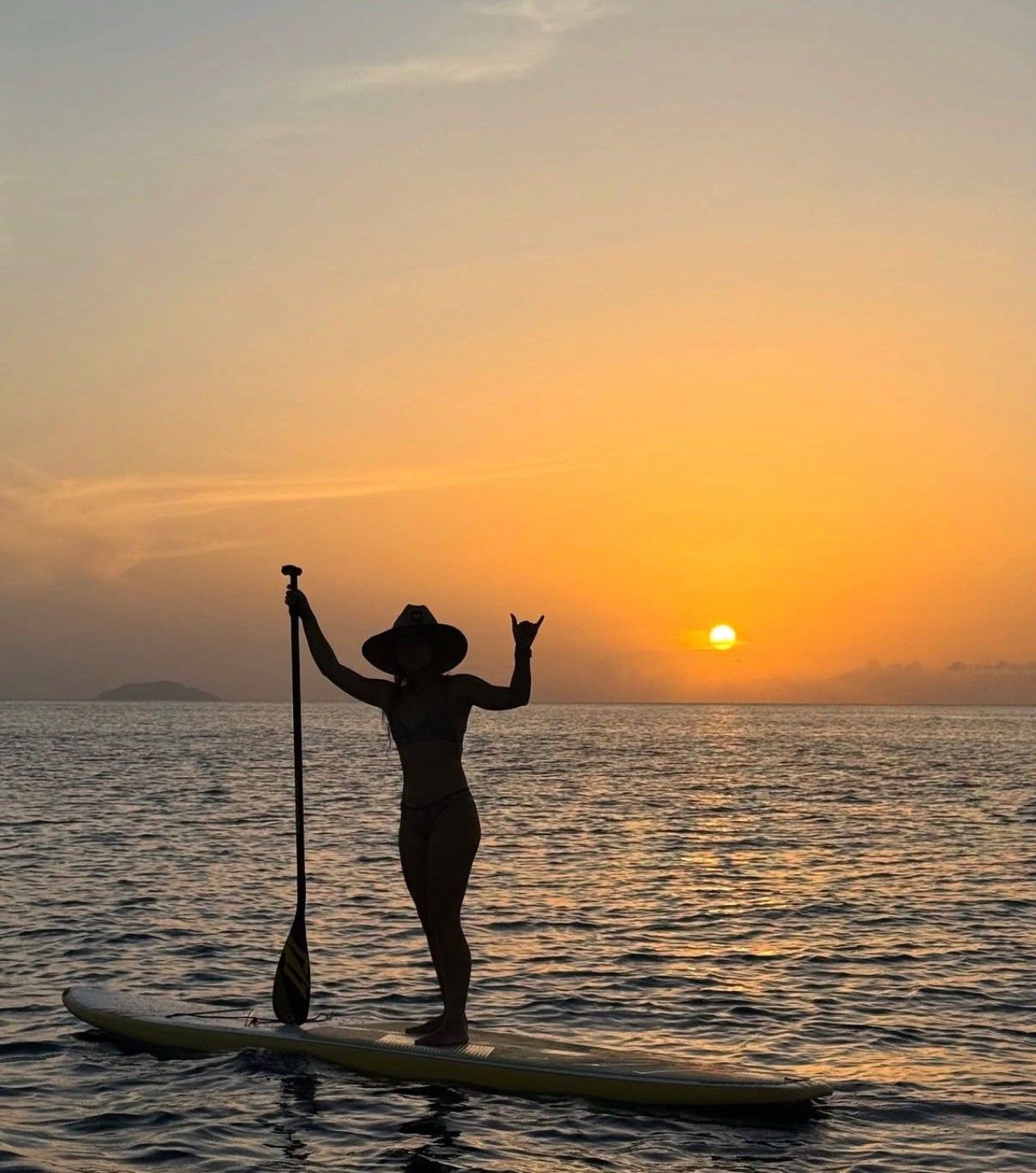 En person står på paddleboard på roligt vand i solnedgangen.