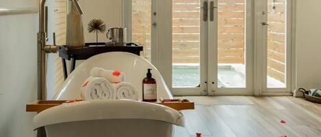 A bathroom with a freestanding bathtub, a wooden floor, and a view of a wooden deck through a sliding glass door.