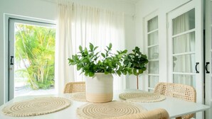 Een eetgedeelte met een witte tafel, geweven stoelen en een potplant.