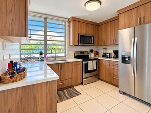 A modern kitchen with wooden cabinets, stainless steel appliances, and a large window.