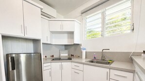 Une cuisine moderne avec des meubles blancs, un réfrigérateur en acier inoxydable, un évier et une fenêtre avec des stores.