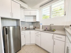 Une cuisine moderne avec des meubles blancs, un réfrigérateur en acier inoxydable, un évier et une fenêtre avec des stores.