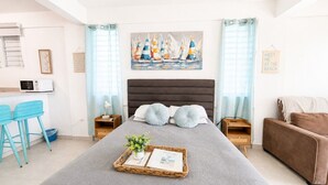 Un dormitorio con cama, un escritorio pequeño, una silla, una mesita de noche y un cuadro colgado en la pared.