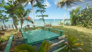 Una terraza de madera con vista al océano, rodeada de vegetación tropical y palmeras.