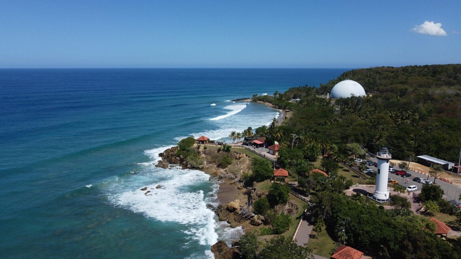 Une zone côtière comprenant un phare, une structure en forme de dôme et une plage avec des vagues.