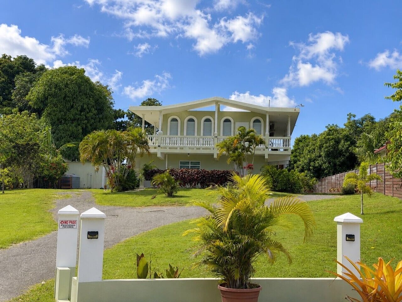 A large, two-story building with a balcony, surrounded by lush greenery and a well-maintained lawn.