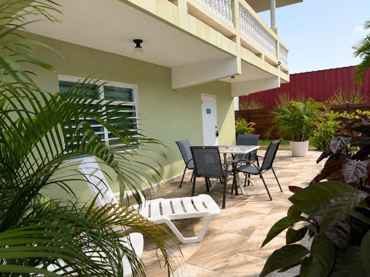 A patio with a table and chairs, a white lounge chair, and potted plants.