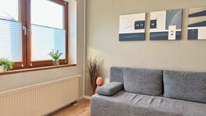 A living room with a grey sofa, a radiator, a window with blinds, and wall art.