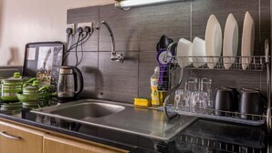 A kitchen with a sink, a coffee maker, and a dish rack with plates and cups.