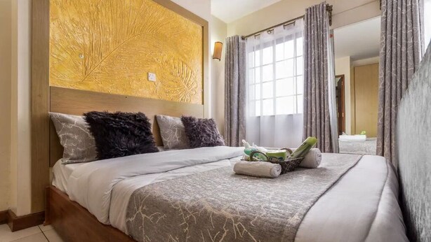 A hotel room with a large bed, a headboard with a textured design, a window with curtains, and a mirror on the wall.